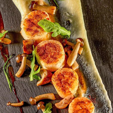 Grand Mercure Dubai City Hotel Exterior photo The photo showcases a beautifully plated dish featuring seared scallops. The scallops are golden brown on the outside and are arranged neatly on a dark slate plate. Accompanying the scallops are small pieces of sautéed mushrooms and a garnish of fres