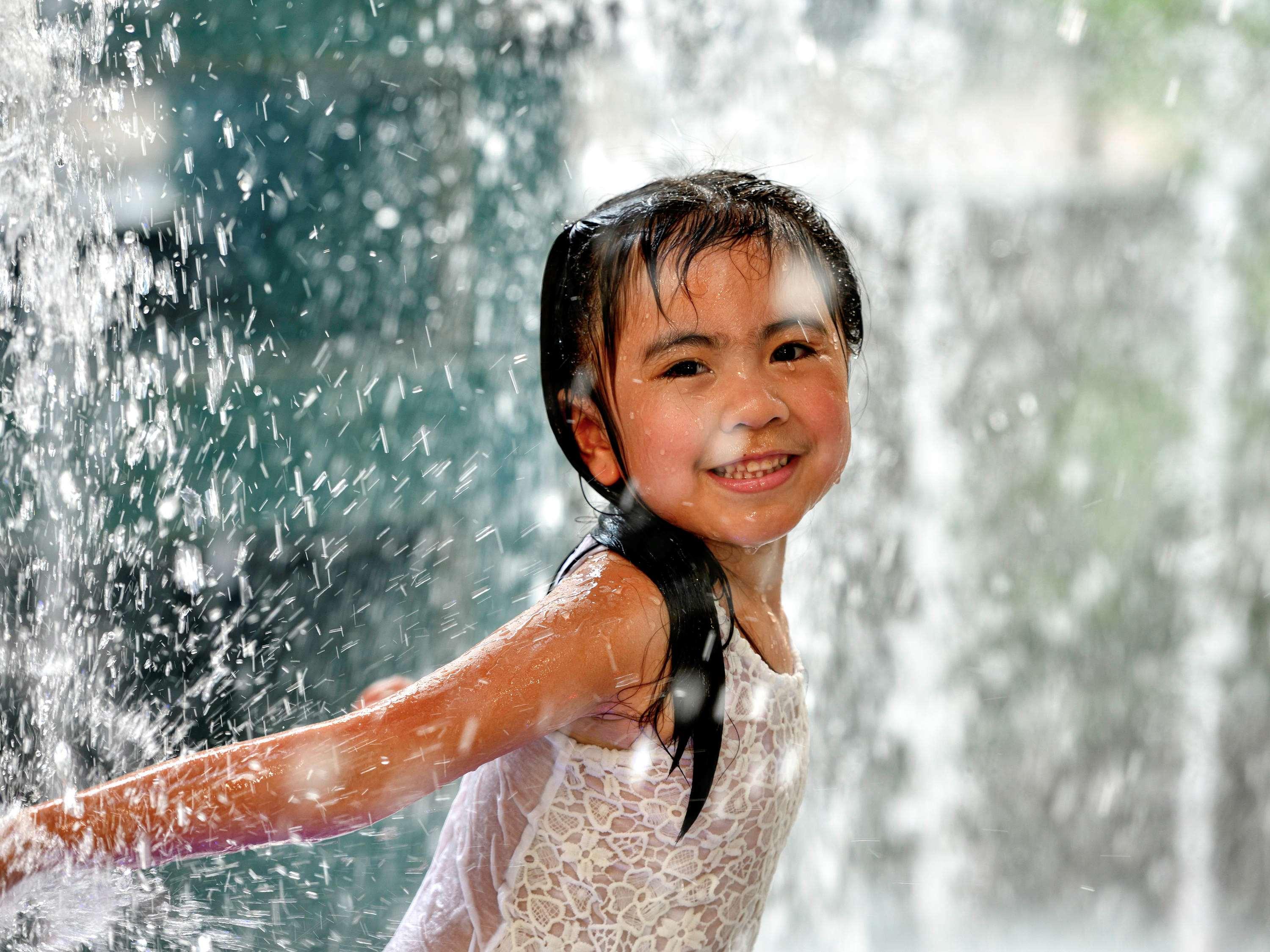 Grand Mercure Dubai City Hotel Exterior photo The photo shows a young girl joyfully playing in a water fountain. She has wet hair and is wearing a light-colored outfit, possibly a dress or swimsuit. The background features splashes of water cascading down, creating a refreshing and playful atmos