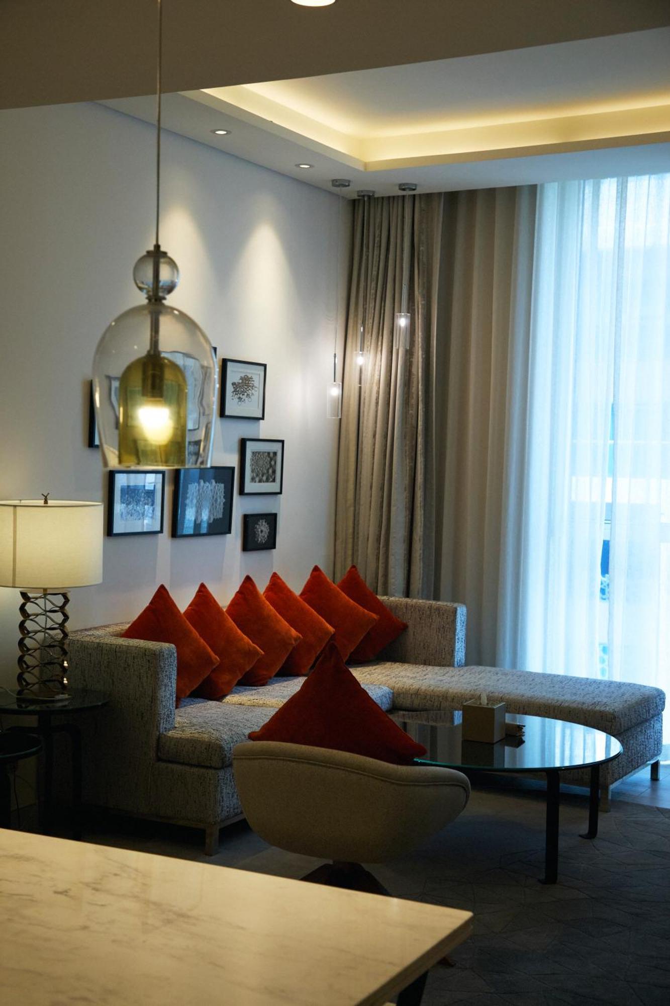 Grand Mercure Dubai City Hotel Exterior photo The photo shows a modern living room area with a stylish design. There is a light-colored couch adorned with several orange cushions that provide a pop of color. On the wall behind the couch, there are various framed artworks, adding an artistic touc