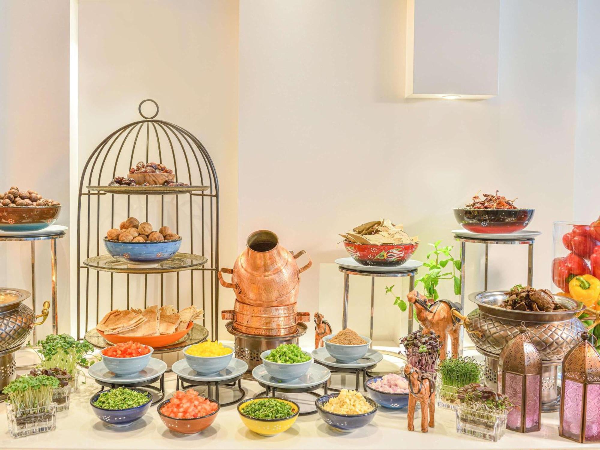 Grand Mercure Dubai City Hotel Exterior photo The photo displays a beautifully arranged buffet setup featuring an assortment of dishes. There are several bowls in various colors filled with different ingredients, including grains, herbs, and toppings. A decorative cage holds additional food item