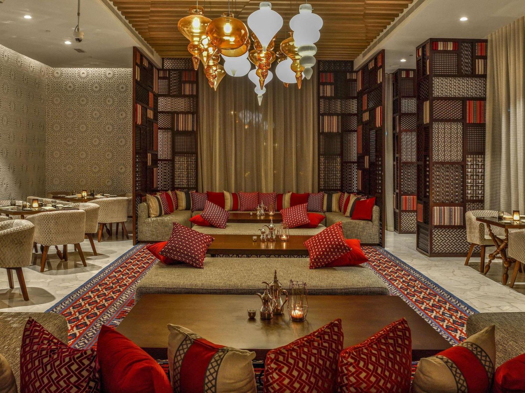 Grand Mercure Dubai City Hotel Exterior photo The photo depicts an elegantly designed dining area with a cozy and inviting atmosphere. The space features plush seating arrangements, including cushions in rich red and patterned fabrics, arranged on the floor and around low tables. The walls are a